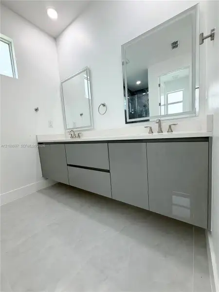 Floating dual vanity with high-gloss gray cabinetry, white stone-finish countertop, undermount sinks, and LED-backlit vanity mirrors