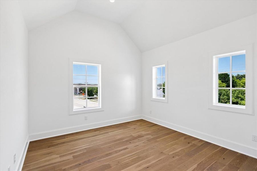 Vaulted ceiling room featuring hardwood flooring and three large windows