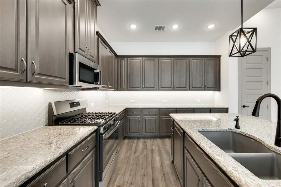 Kitchen with appliances with stainless steel finishes, light wood-type flooring, decorative light fixtures, dark brown cabinetry, and sink