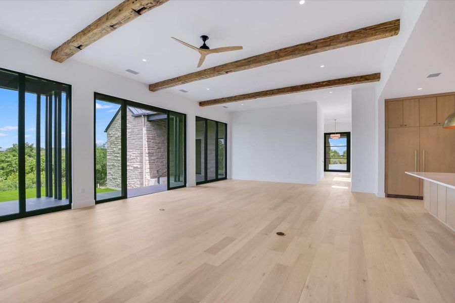 An open-concept living area with exposed timber beams and wide plank wood flooring offers serene views through expansive sliding glass doors.