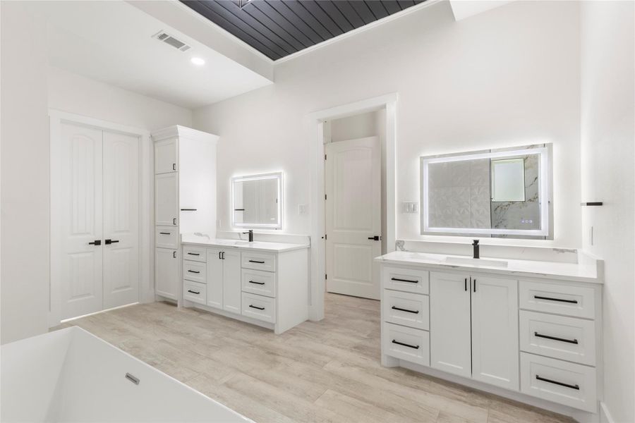 Primary bathroom showcasing separate vanities, lighted mirrors, black hardware and a shiplap ceiling. Primary bathroom showcasing separate vanities, lighted mirrors, black hardware and a shiplap ceiling.