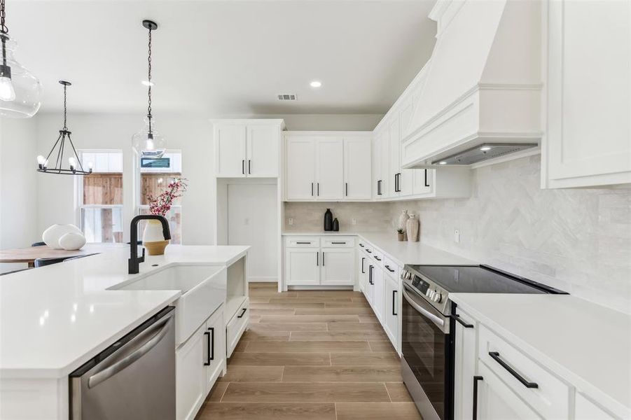 Kitchen with appliances with stainless steel finishes, decorative backsplash, white cabinets, custom exhaust hood, and hanging light fixtures