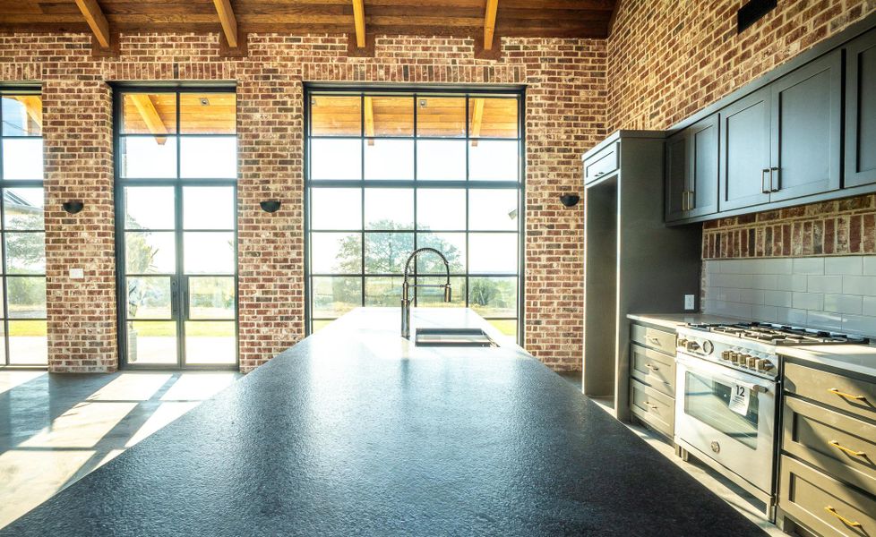Kitchen featuring brick wall, stainless steel gas stove, and beamed ceiling