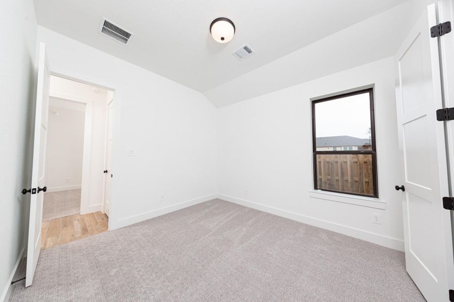 This well appointed secondary bedroom features a sloped ceiling, plush carpet flooring, neutral-toned walls, a large window, and a walk-in closet.