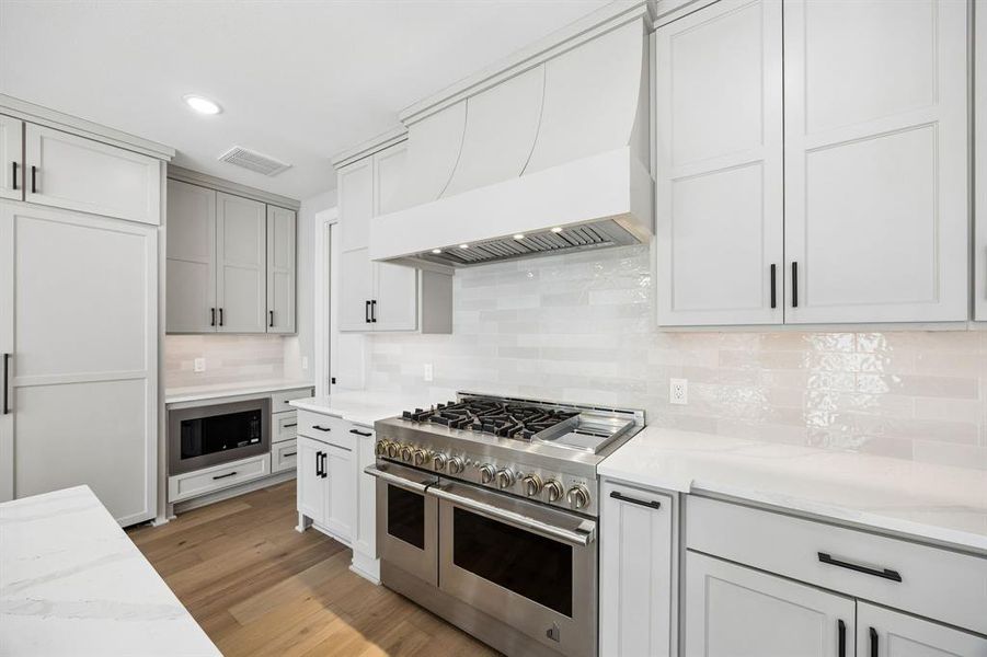 Kitchen with stainless steel appliances, recessed lighting, backsplash, light wood-type flooring, and light stone countertops Kitchen with stainless steel appliances, recessed lighting, backsplash, light wood-type flooring, and light stone countertops