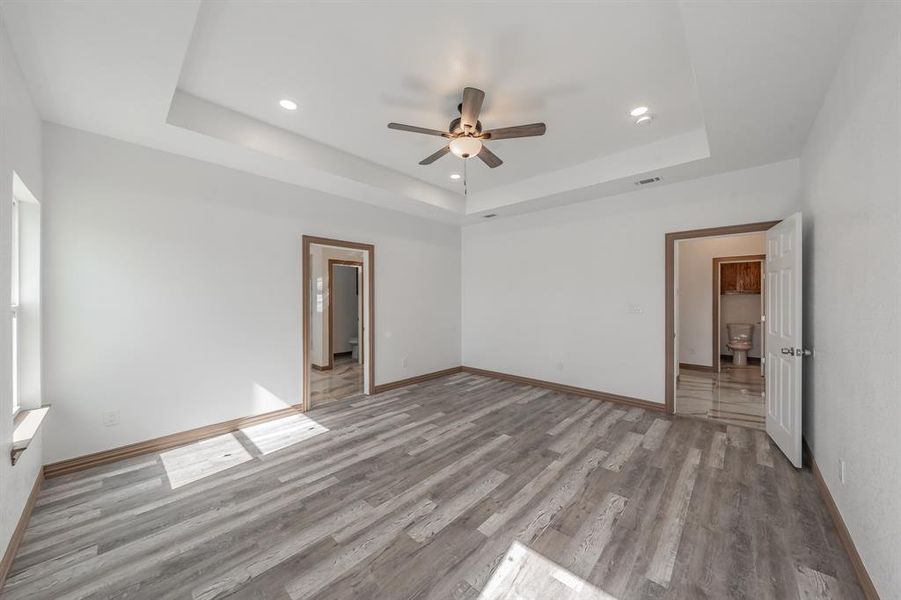 Empty room with light wood-style flooring, recessed lighting, visible vents, baseboards, and a tray ceiling