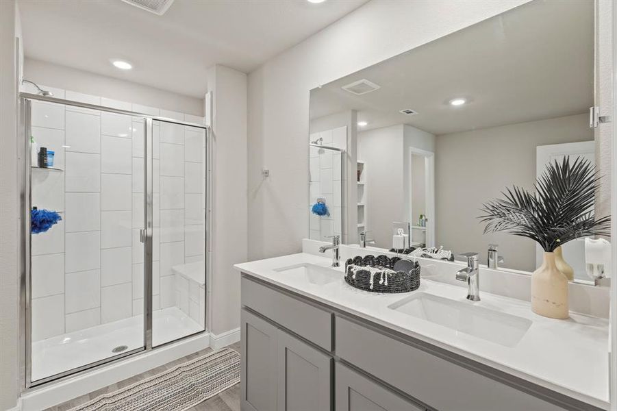 Bathroom featuring a dual-sink vanity with light gray cabinetry, a large frameless mirror, and a walk-in shower with clear glass enclosure and built-in bench Bathroom featuring a dual-sink vanity with light gray cabinetry, a large frameless mirror, and a walk-in shower with clear glass enclosure and built-in bench