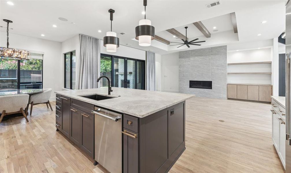 Kitchen with a fireplace, sink, decorative light fixtures, light hardwood / wood-style floors, and an island with sink