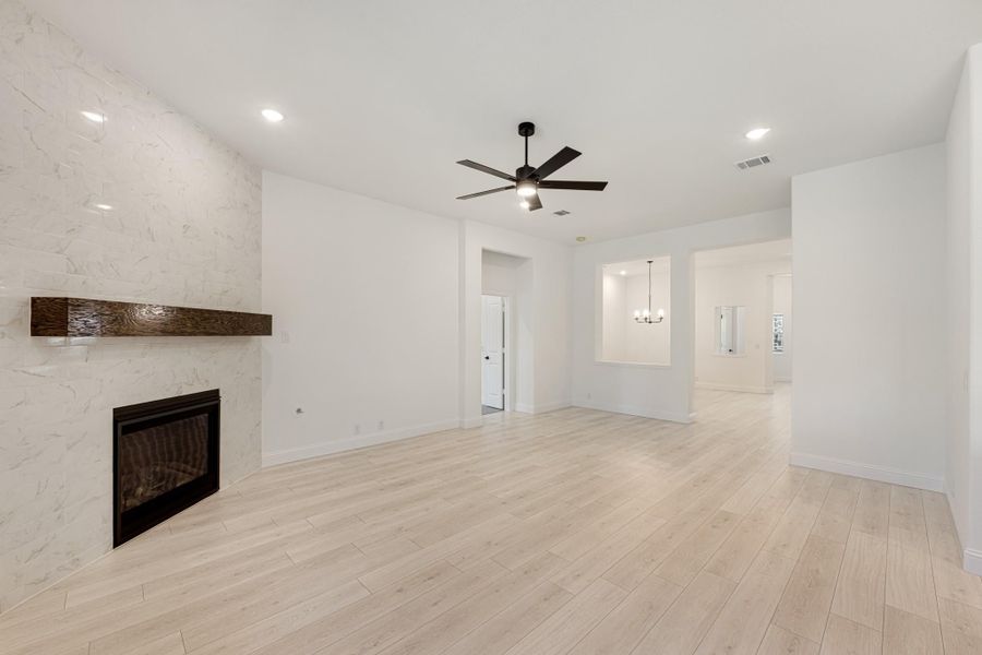 Open living room with marble tile fireplace, wood mantel, ceiling fan, and light hardwood floors
