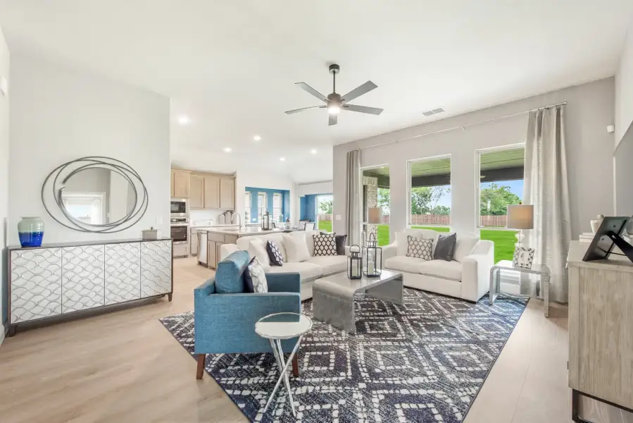 Open-concept living room with ceiling fan, light wood floors, and kitchen visible in background