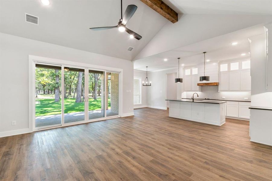 Unfurnished living room with ceiling fan with notable chandelier, beamed ceiling, hardwood / wood-style flooring, sink, and high vaulted ceiling