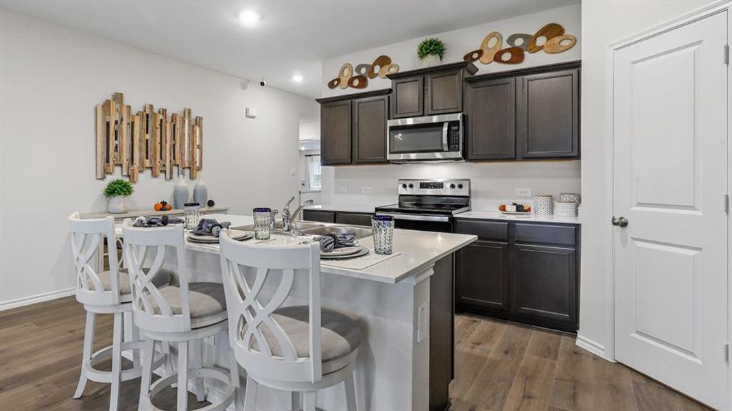 Kitchen with dark wood finish cabinets, light countertops, a center island with sink, a kitchen breakfast bar, and stainless steel appliances Kitchen with dark wood finish cabinets, light countertops, a center island with sink, a kitchen breakfast bar, and stainless steel appliances