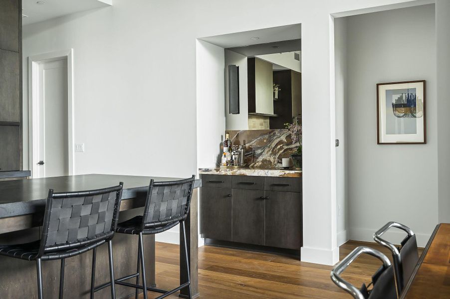 Indoor dry bar featuring dark wood-style floors, decorative backsplash, light stone countertops, and dark brown cabinets Indoor dry bar featuring dark wood-style floors, decorative backsplash, light stone countertops, and dark brown cabinets