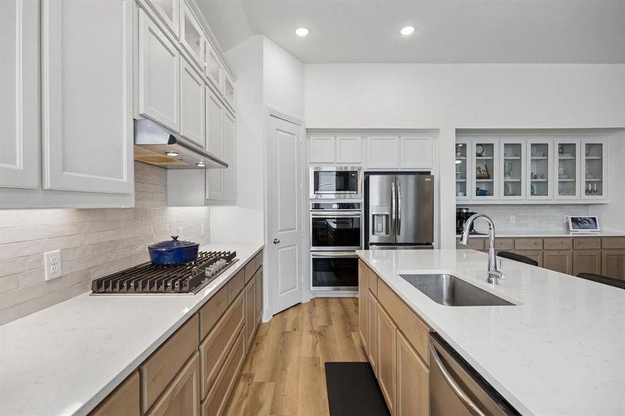 Gourmet kitchen featuring a gas cooktop, stainless steel appliances, white cabinetry, light wood-finish lower cabinetry, and a large center island with an undermount sink