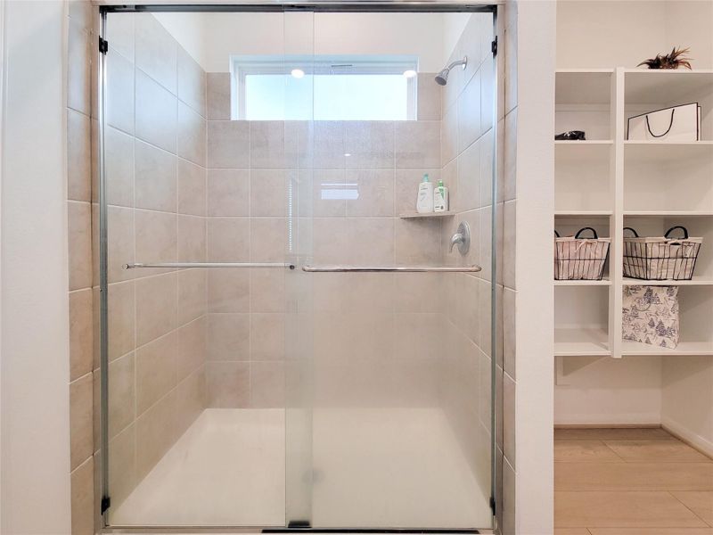 Modern bathroom with a spacious tiled shower featuring a glass door and built-in shelf. Adjacent open shelving provides convenient storage options.