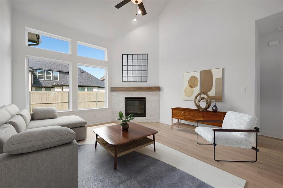 Living room with a glass covered fireplace, light wood-type flooring, vaulted ceiling, ceiling fan, and recessed lighting
