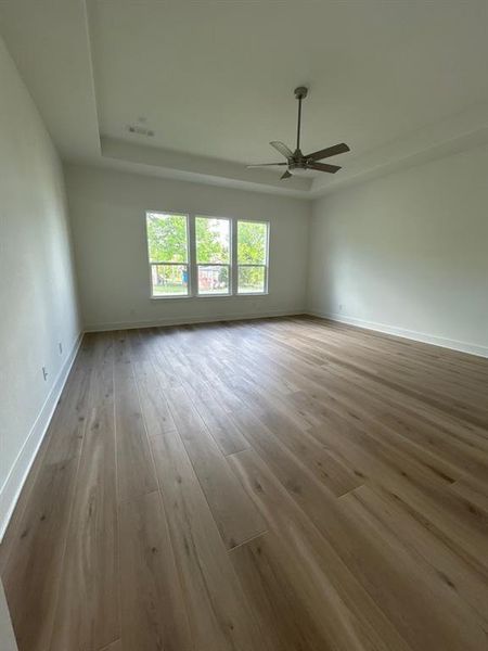 Spare room with light wood-type flooring, a ceiling fan, and a raised ceiling