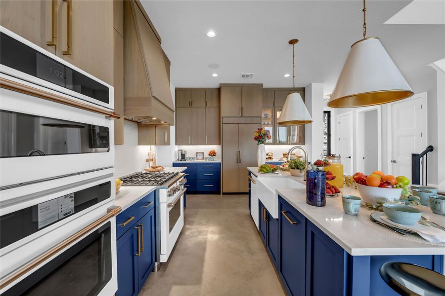 Gourmet kitchen featuring dual wall ovens, a large center island with a farmhouse sink, stone countertops, and contrasting blue and wood-finish cabinetry