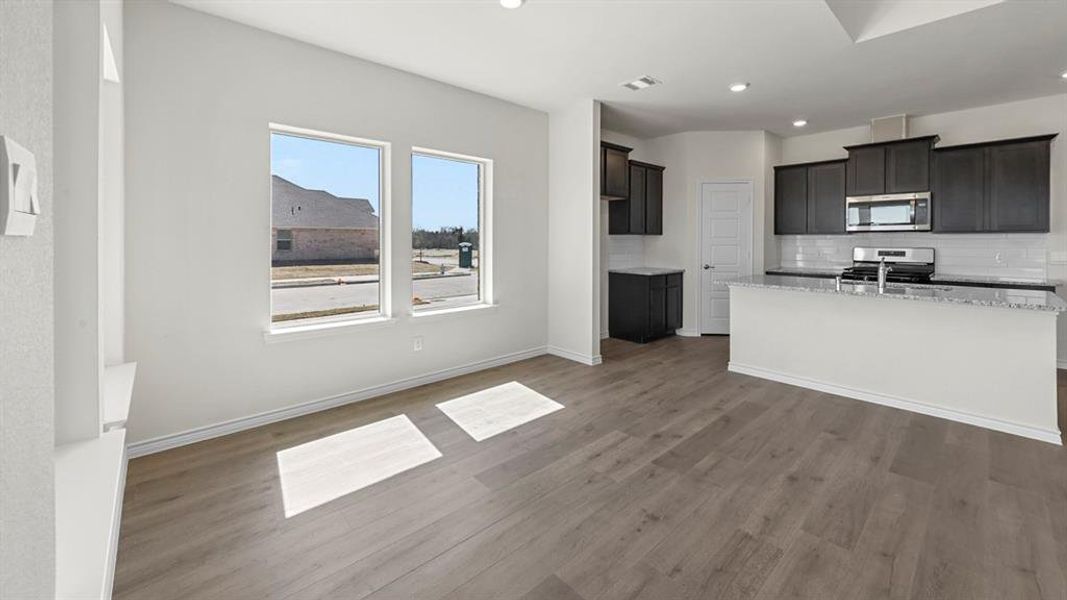 Kitchen featuring light stone counters, tasteful backsplash, appliances with stainless steel finishes, a center island with sink, and recessed lighting