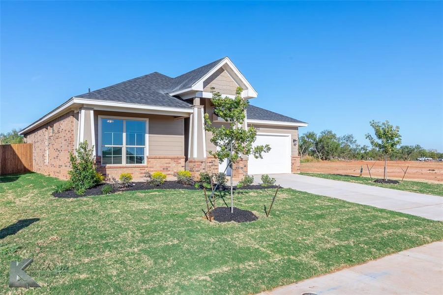 Craftsman-style home with a shingled roof, brick siding, driveway, and an attached garage