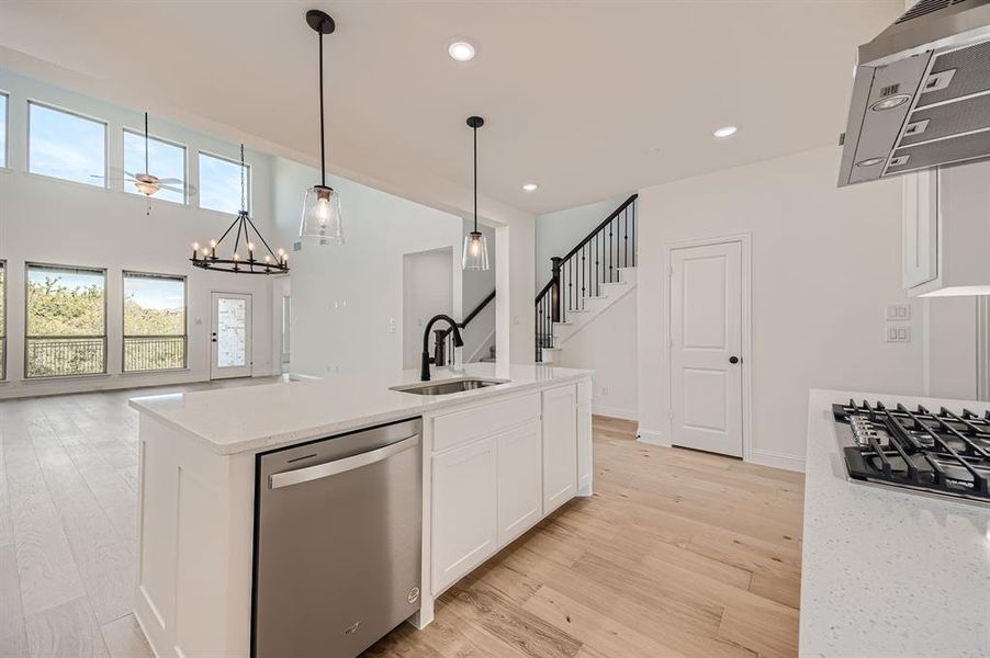 Kitchen with light hardwood / wood-style floors, white cabinets, a center island with sink, stainless steel dishwasher, and sink