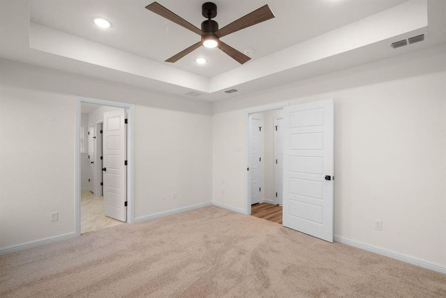 Unfurnished bedroom with a tray ceiling, ceiling fan, and light colored carpet Unfurnished bedroom with a tray ceiling, ceiling fan, and light colored carpet