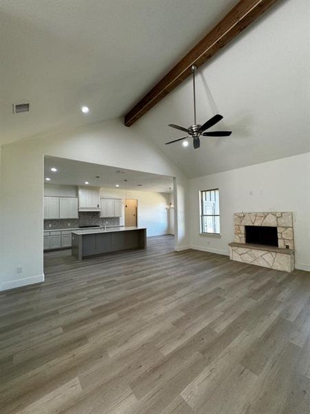 Unfurnished living room featuring beamed ceiling, a fireplace, high vaulted ceiling, wood-type flooring, and ceiling fan