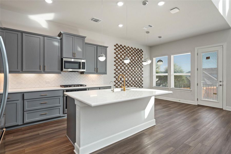 Modern cabinetry and a central island highlight this open-concept culinary space with rich wood-style flooring.