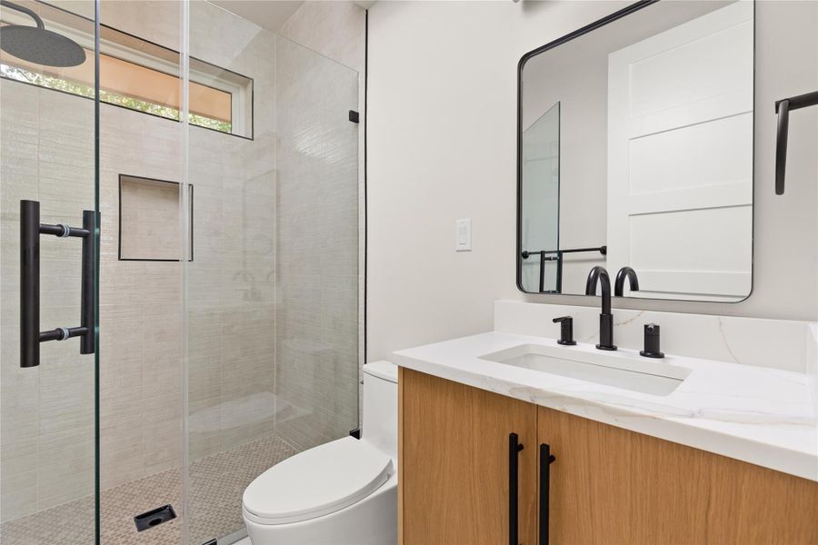 Modern stone counters and a sleek glass-enclosed shower define this refined bathroom.