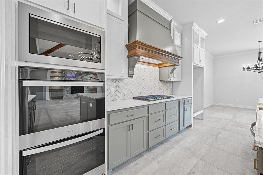 Kitchen with stainless steel appliances, backsplash, glass insert cabinets, crown molding, and a chandelier Kitchen with stainless steel appliances, backsplash, glass insert cabinets, crown molding, and a chandelier