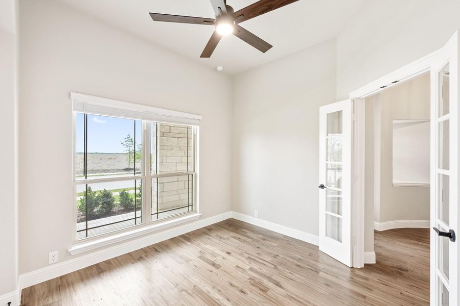 Empty room with hardwood floors, ceiling fan, large window, and French doors leading to adjacent space Empty room with hardwood floors, ceiling fan, large window, and French doors leading to adjacent space