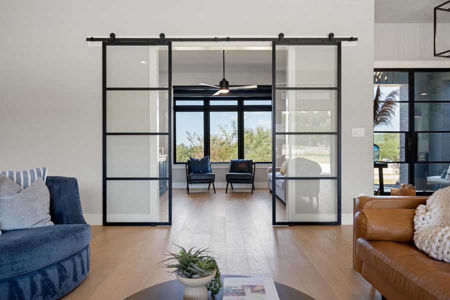 Double sliding glass barn doors connect light-filled living spaces over warm hardwood floors.