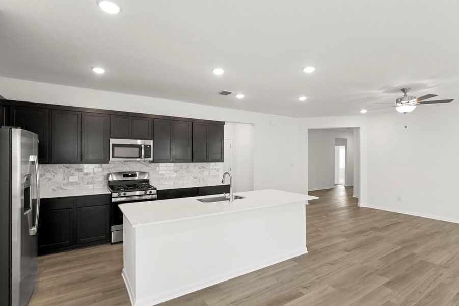 Kitchen featuring appliances with stainless steel finishes, light wood-type flooring, recessed lighting, decorative backsplash, and a center island with sink