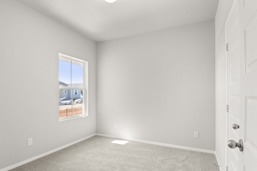 Image of a bedroom with tan carpeting, light grey walls and a window