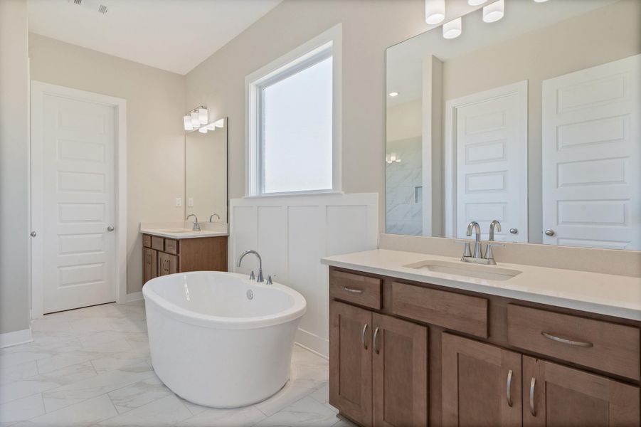 Bathroom featuring two vanities, light marble finish floors, and a freestanding tub