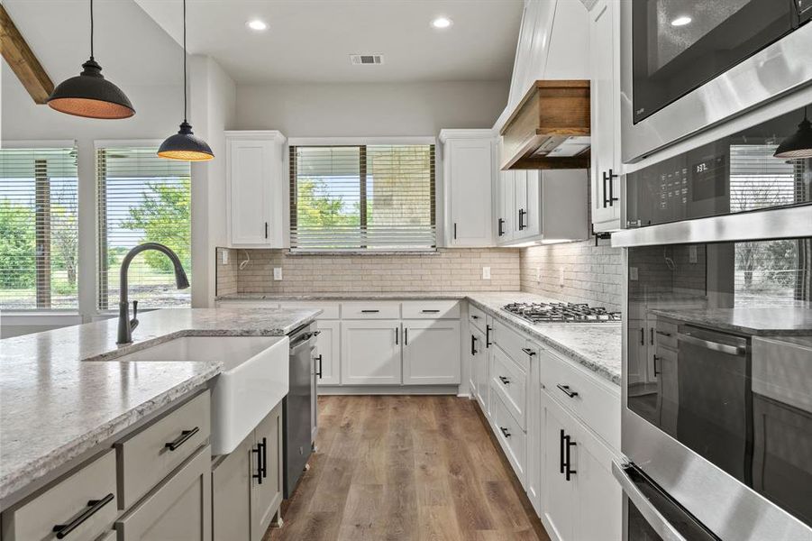 Kitchen with white cabinets, decorative backsplash, stainless steel appliances, hanging light fixtures, and light stone countertops Kitchen with white cabinets, decorative backsplash, stainless steel appliances, hanging light fixtures, and light stone countertops