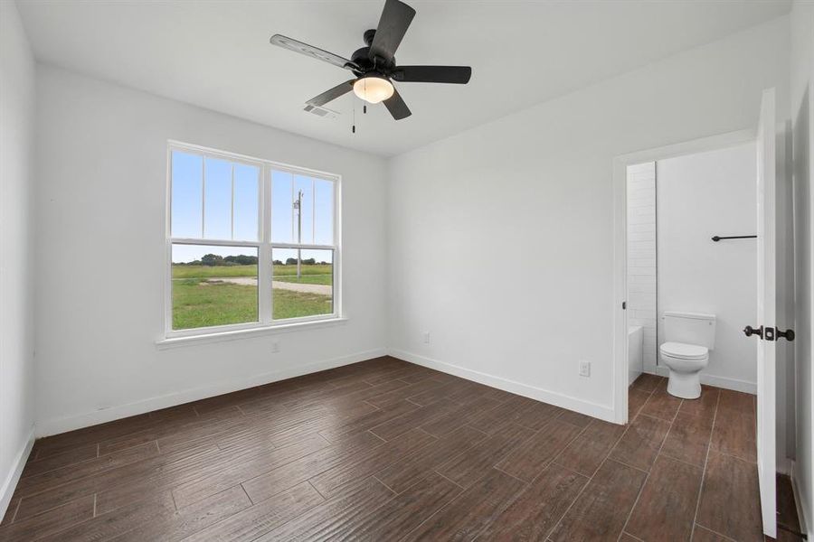 Unfurnished bedroom with dark wood-type flooring, ceiling fan, and connected bathroom