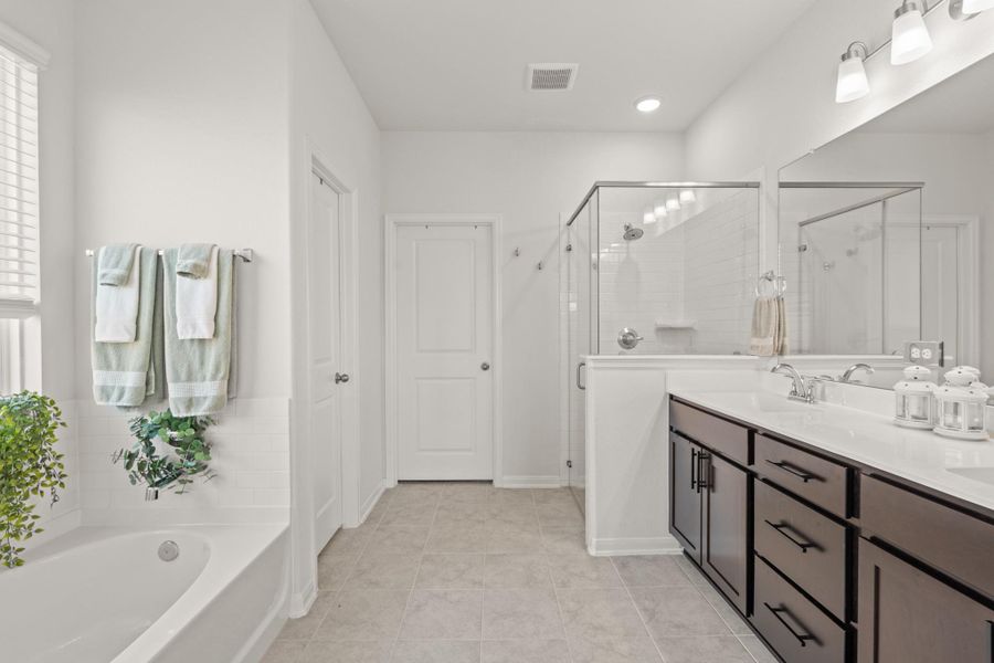 Indulge in the spaciousness of this primary bathroom featuring dual vanities, a walk-in shower with mud-set tile and glass surround, large soaking tub, and a bright window that fills the space with natural light