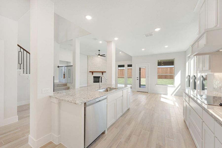 Open kitchen with white cabinets, granite island, and view into living room with stone fireplace