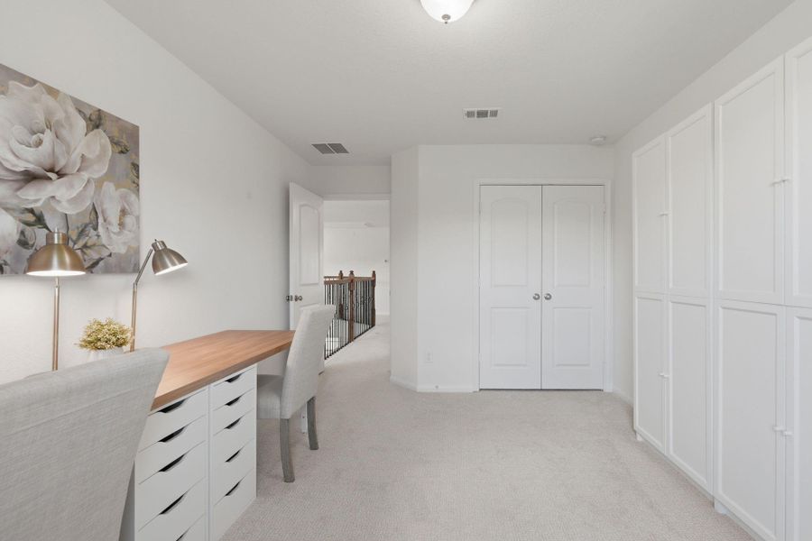 This bright, carpeted room features a built-in desk with ample storage, ideal for a home office. It has a double-door closet and opens to a hallway with elegant railing. Perfect for a quiet workspace.