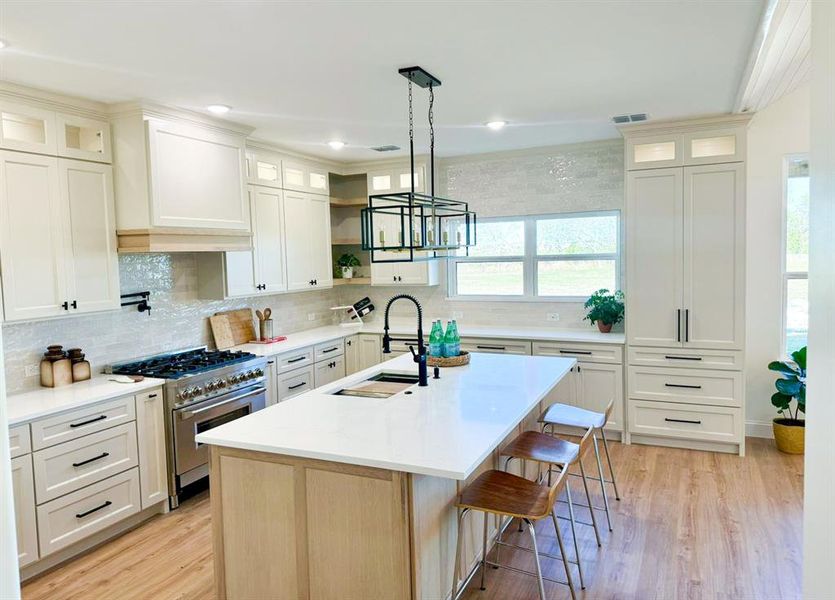 Kitchen with pendant lighting, light hardwood / wood-style flooring, high end stainless steel range, and a kitchen island with sink