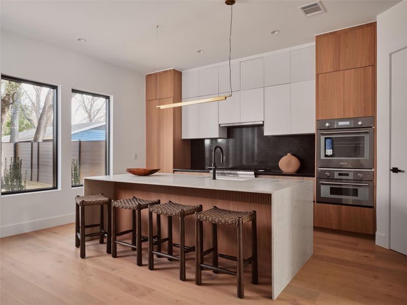 Dual tone kitchen with two tone cabinets, modern cabinets, light stone countertops, stainless steel double oven, and a breakfast bar