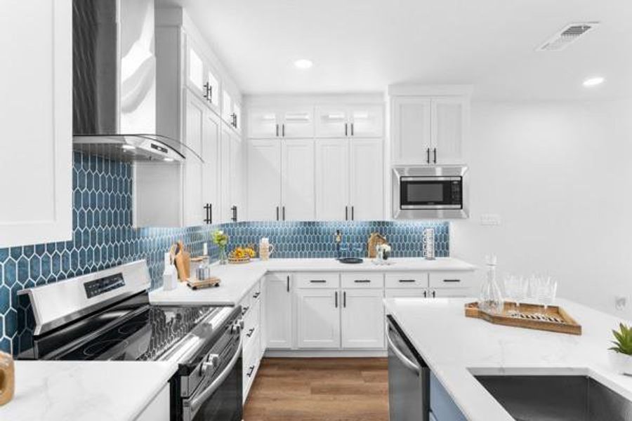 Kitchen with stainless steel appliances, white cabinetry, light stone counters, wall chimney exhaust hood, and dark wood-type flooring Kitchen with stainless steel appliances, white cabinetry, light stone counters, wall chimney exhaust hood, and dark wood-type flooring