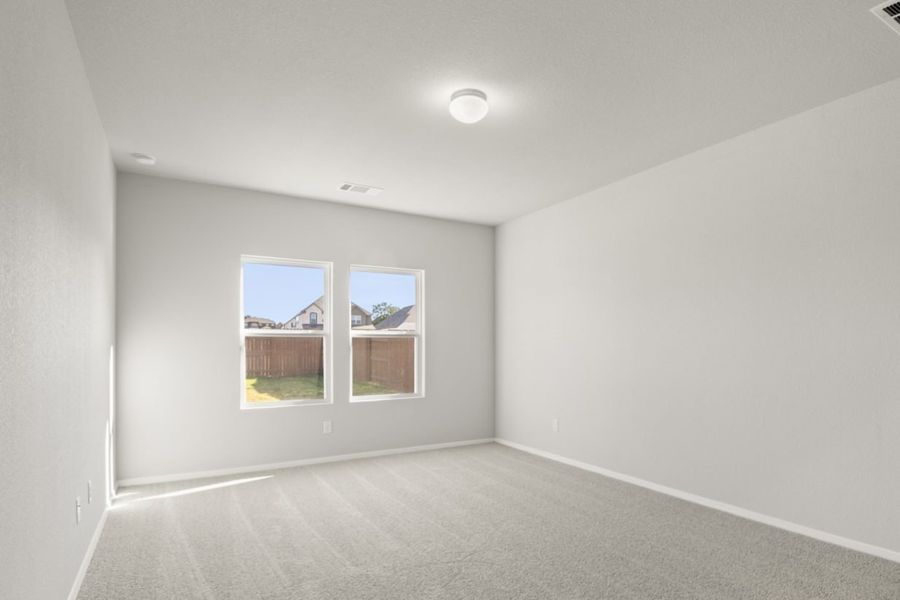 Image of a primary bedroom with tan carpeting and light grey painted walls with two windows Image of a primary bedroom with tan carpeting and light grey painted walls with two windows