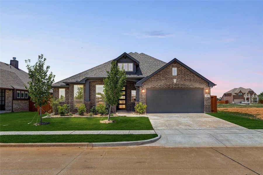Single-story brick home with two-car garage, landscaped front yard, and concrete driveway at dusk