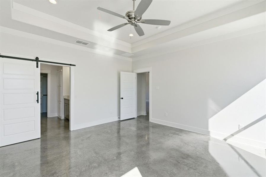 Unfurnished bedroom featuring a barn door, finished concrete floors, a raised ceiling, recessed lighting, and ceiling fan