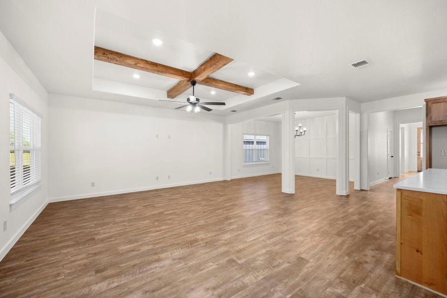 A spacious living area features wood-look flooring and a distinctive coffered ceiling with exposed beams.