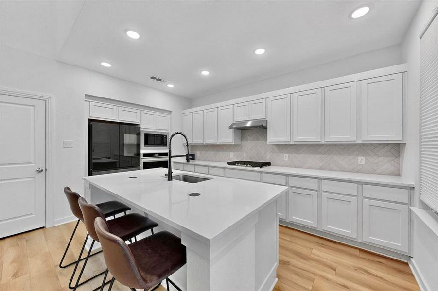 Kitchen with white cabinets, light wood finished floors, decorative backsplash, black appliances, and recessed lighting Kitchen with white cabinets, light wood finished floors, decorative backsplash, black appliances, and recessed lighting