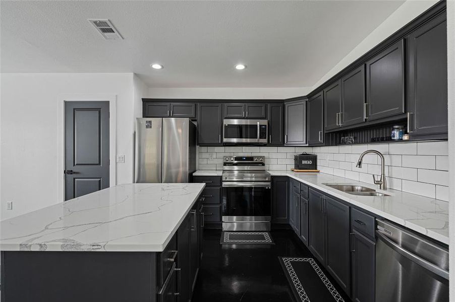 Kitchen with stainless steel appliances, light stone countertops, and a center island