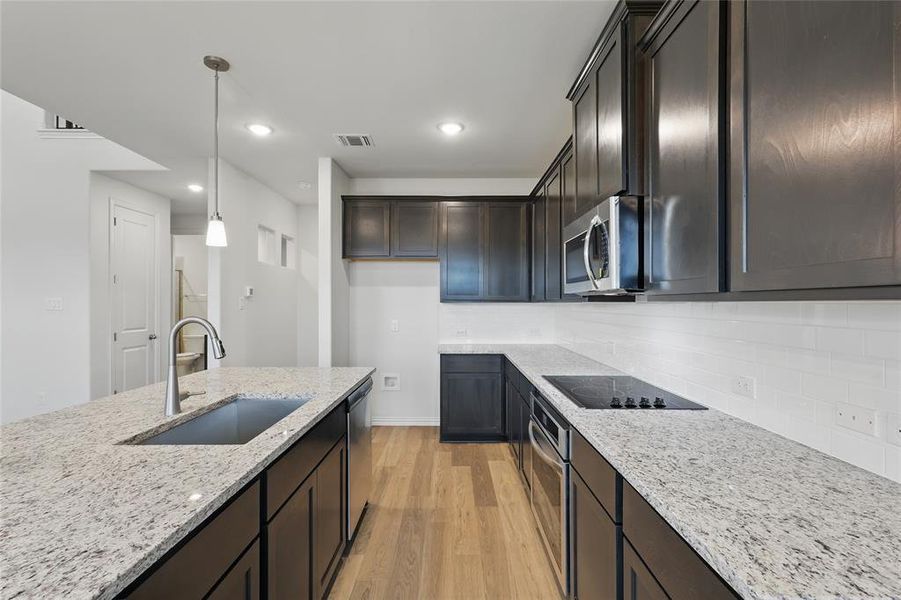 Kitchen featuring stainless steel appliances, a sink, light wood finished floors, light stone countertops, and decorative light fixtures Kitchen featuring stainless steel appliances, a sink, light wood finished floors, light stone countertops, and decorative light fixtures